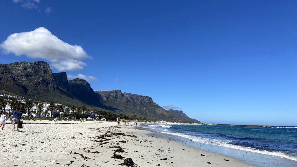 Camps Bay beach in Cape Town with the Twelve Apostles mountain range rising behind it under a blue sky